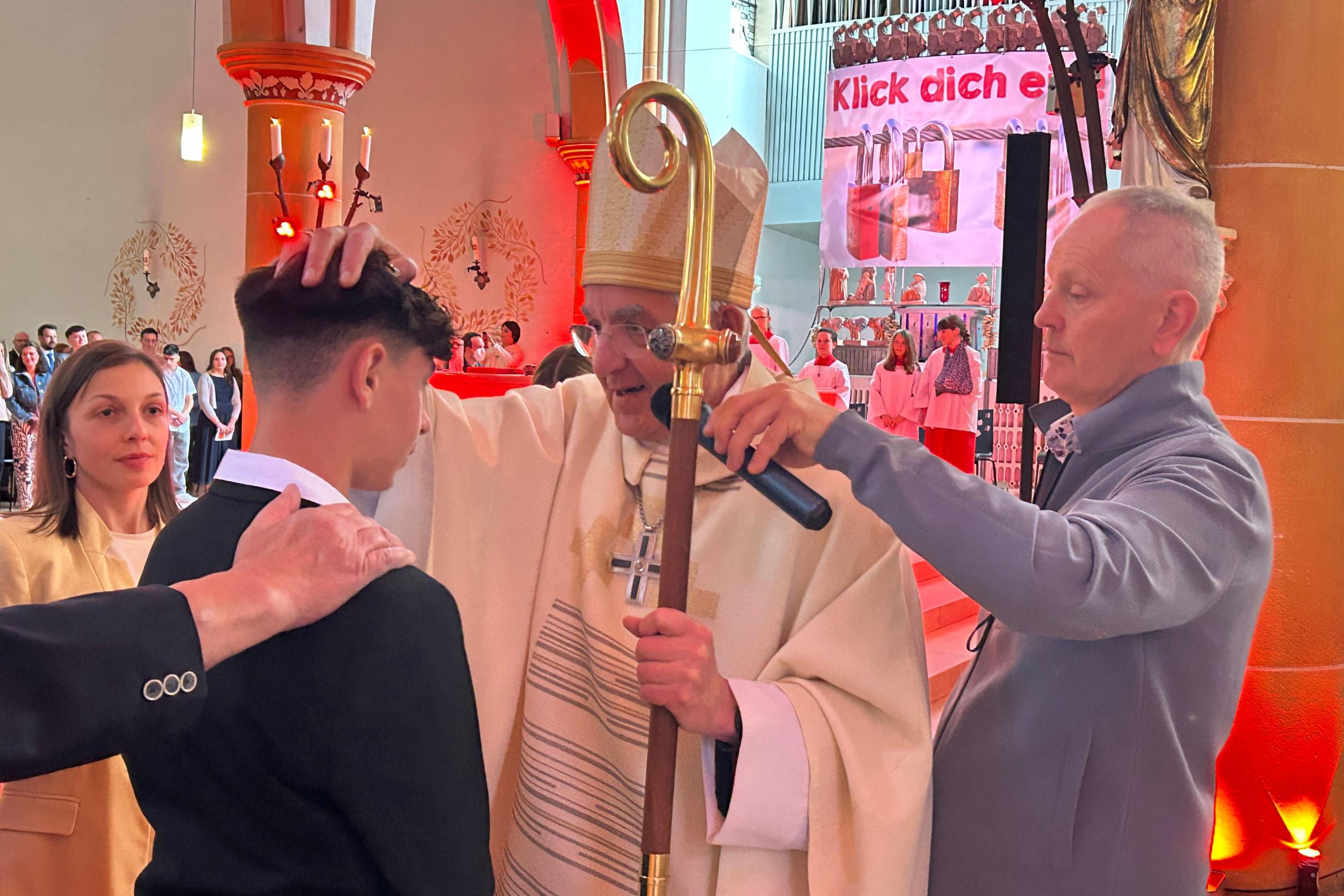Ein Weihbischof mit Bischofsstab legt einem jungen Mann die Hand zur Firmung auf